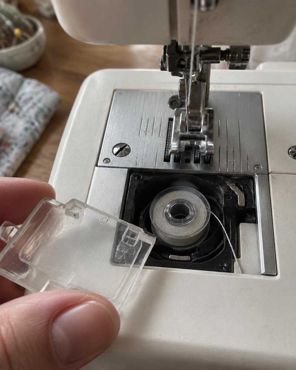 Bobina transparente deitada no compartimento superior aberto de uma máquina doméstica
