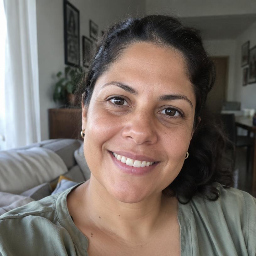 Foto de perfil de Márcia, mulher de cabelo escuro preso, sorrindo na sala de casa